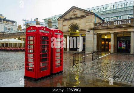 London's iconic red telephone booths, telephone boxes, in the popular Covent Garden Market on a rainy day. The streets are empty and shops are closed. Stock Photo