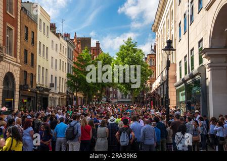 Crowds of people gather by Covent Garden Market, a popular square, to watch street performers on a beautiful sunny day in London. Historic fun square! Stock Photo