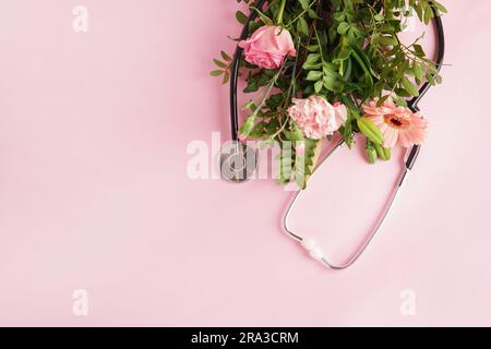 stethoscope and bouquet of flowers and green leaves on light pink background. Top view with copy space. National Doctor's day. Happy nurse day Stock Photo