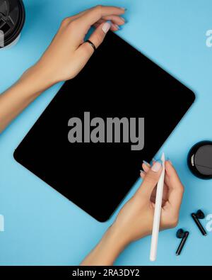 Flat lay top view womans hands holding digital tablet with blank screen on blue background. Home office workspace Stock Photo