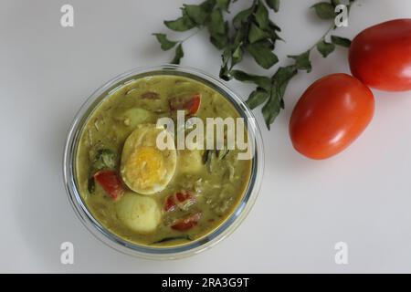 Egg curry. Egg masala curry prepared in Kerala style using coconut milk, tomatoes and onions. Shot on white background along with tomatoes and curry l Stock Photo