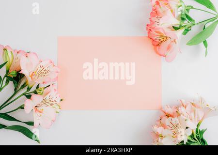 Beautiful Alstroemeria pink flowers and blank card. Festive background, mockup. Top view, flat lay. Stock Photo