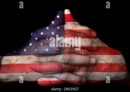 Closeup of man's praying hands with American flag overlay isolated on black background Stock Photo