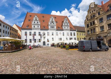 The late-Gothic Meissen town hall, built between 1472 and 1480, dominates the market square of the old town with its steep gabled roof and three dormers, Saxony, Germany. Guests sit at café tables under parasols, a delivery van is parked on the cobblestones. Stock Photo