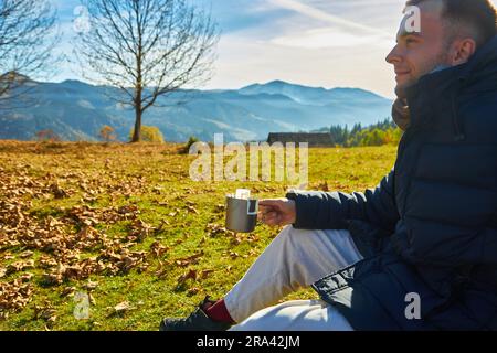 A tourist drinks coffee against the backdrop of beautiful autumn mountains and nature Stock Photo