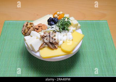 Delicious cheese mix with grapes, jam, snacks, crackers, walnuts and vine on a wooden board. Dinner or aperitif concept. Exquisite cheese plate, wine Stock Photo