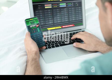 Man betting on sports using laptop and smartphone at home, closeup. Bookmaker websites on displays Stock Photo