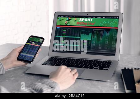 Woman betting on sports using smartphone and laptop at table, closeup. Bookmaker websites on displays Stock Photo