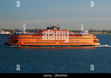 The orange Staten Island Ferry crosses New York Harbor bringing commuters and tourists on a boat between Staten Island and Manhattan in New York City Stock Photo