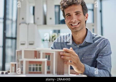 young caucasian engineer man making building model with the use of drawings and notes in office. Stock Photo