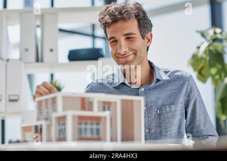 young caucasian engineer man making building model with the use of drawings and notes in office. smart designer assembles a complex structure Stock Photo