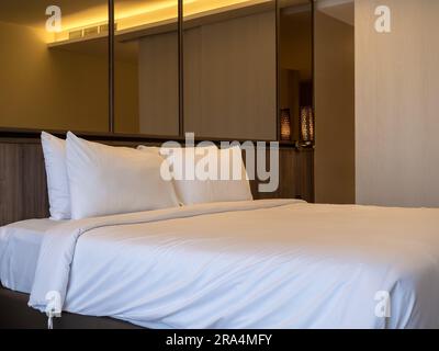 Couple white pillow on the empty bed with white duvet on luxury modern design interior with large mirror wall background in hotel bedroom. Two soft an Stock Photo