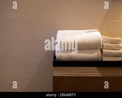 White clean folded towels in the black tray on wooden table white marble tiles wall background with copy space. Towel set reserved for the guest in ho Stock Photo
