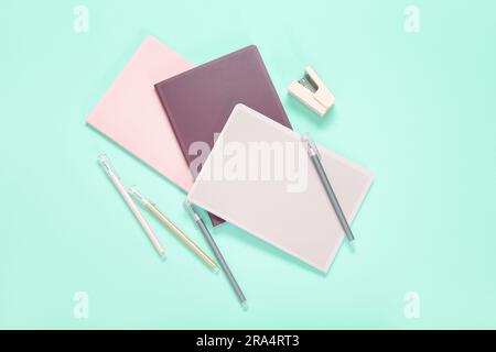 Different colorful notebooks with pens and stapler on turquoise background Stock Photo