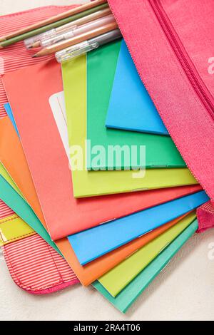 School backpack with different colorful notebooks, pens and pencils on grunge light background Stock Photo