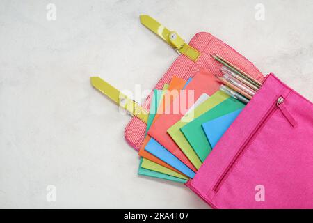 School backpack with different colorful notebooks, pens and pencils on grunge light background Stock Photo