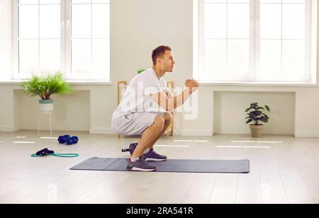 Sporty young man doing squats during an active fitness workout at the gym or at home Stock Photo