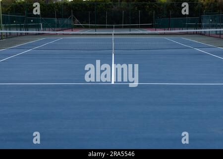 Empty blue surfaced outdoor tennis court with net and white markings, copy space Stock Photo