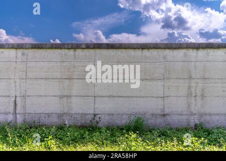 Concrete wall with blue sky and clouds and green grass at the base, background textured, copy space Stock Photo