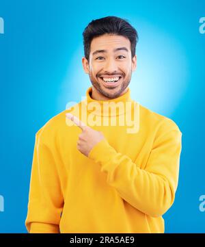 Man, point and smile in studio portrait with choice, fashion and promotion with excited face by blue background. Young Indian guy, gen z student and Stock Photo