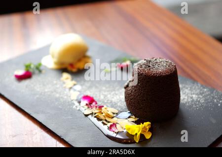 Molten chocolate cake and vanilla ice cream ball with almond slices on black slate plate Stock Photo