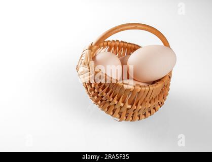 Three chicken eggs in a small wicker basket on a white background. Stock Photo