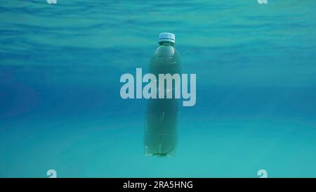 Green plastic bottle drifting under surface of blue water. Plastic pollution of Ocean, Discarded plastic bottle floats underwater in sunlight, Red Stock Photo
