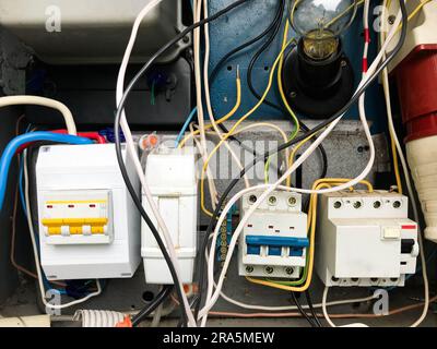 homemade electrical panel. wires and special meters in white. switches, automatic machines in yellow. many wires intertwined with each other. economic Stock Photo