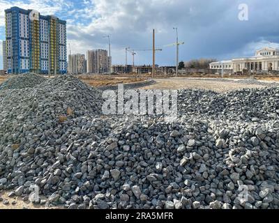 Large gray stones, rubble from industrial road construction and a view of new buildings with cranes at the construction site.