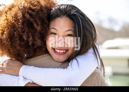 Close up of a young happy woman hugging a curly hair man. Lovely lady smiling while embracing a guy outdoors. Stock Photo