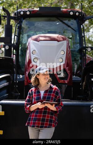 Woman farmer with a digital tablet on the background of an agricultural tractor. Stock Photo