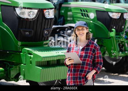 Woman farmer with a digital tablet on the background of an agricultural tractor. Stock Photo