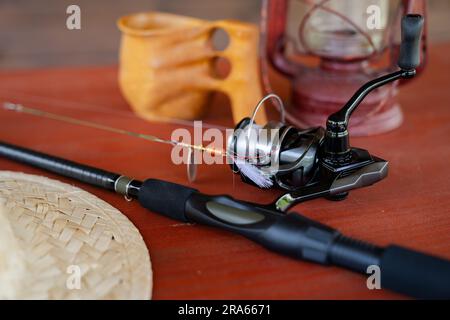 Close-up of spinning rod, straw hat, lantern and mug on wooden table Stock Photo
