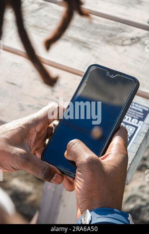 top view of unrecognizable black man hands with a blue watch, using a phone outdoors at sunset, technology conecpt, copy space. Stock Photo