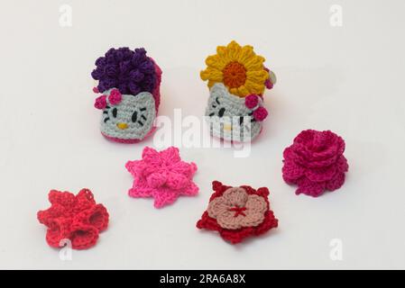 shoes with faces for a newborn and multi-colored flowers, crocheted, on a white background Stock Photo