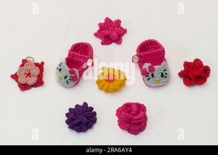 shoes with faces for a newborn and multi-colored flowers, crocheted, on a white background Stock Photo