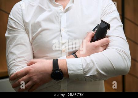 Barber in a light shirt holds clipper in his hands Stock Photo