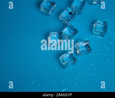 Ice cubes with water drops scattered on a blue background, top view Stock Photo