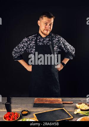 Chef standing next to cutting board with vegetables on it, wearing apron Stock Photo