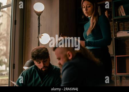Two male coworkers discussing daily task while working remotely. Their female blonde colleague is standing and looking at them Stock Photo