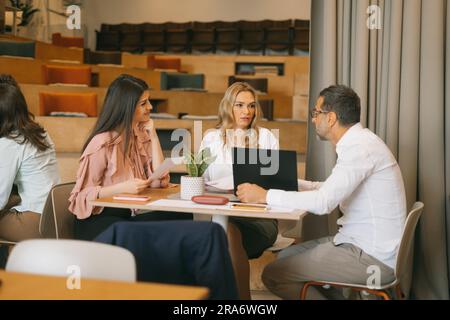 Two middle-aged businesswomen listening to their male colleague explaining project details Stock Photo
