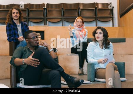Diverse team having a presentation at work. Young, multiracial colleagues listening to their coworker giving ideas for expanding the project to get mo Stock Photo