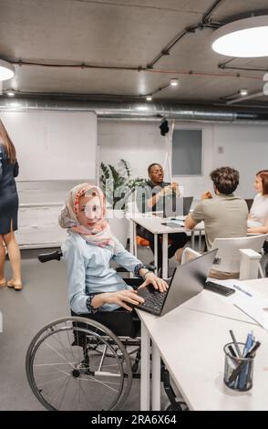 Paralyzed businesswoman in wheelchair was distracted by something while working on the lap top at modern office room Stock Photo