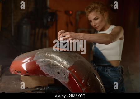 Young woman doing hard job at motorcycle garage using grinder Stock Photo