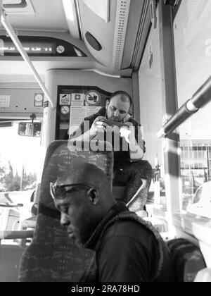 black and white young man sitting on public bus and playing with video games, Valletta, Malta Stock Photo