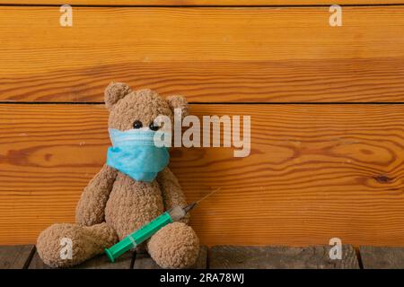 baby brown teddy bear with a syringe and a medical mask during the pandemic period lies on a table Stock Photo