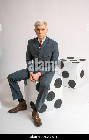 Young man with suit sitting on a giant dice Stock Photo - Alamy