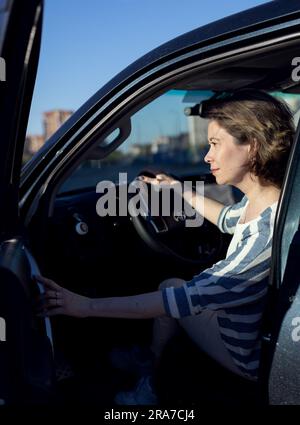 a girl sits in her car and holds and is going to go Stock Photo