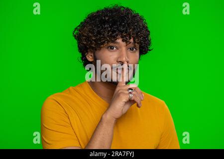 Shh be quiet please. Young indian man presses index finger to lips makes silence gesture sign do not tells secret, stop gossip. Handsome bearded hindu guy isolated alone on chroma key background Stock Photo