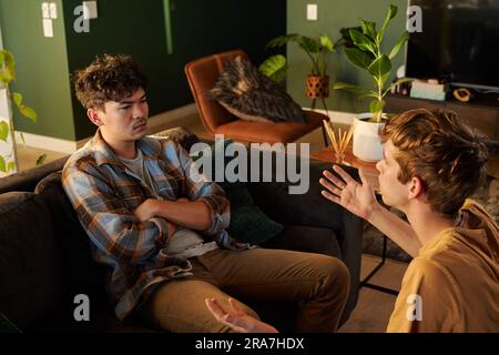 Young gay couple in casual clothing arguing and gesturing in living room at home Stock Photo